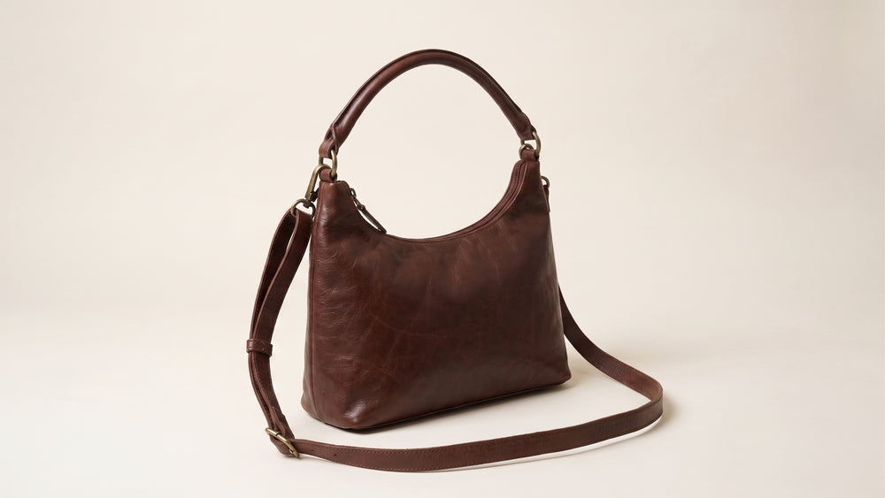 Brown leather handbag featuring an adjustable strap laid out on a marble surface