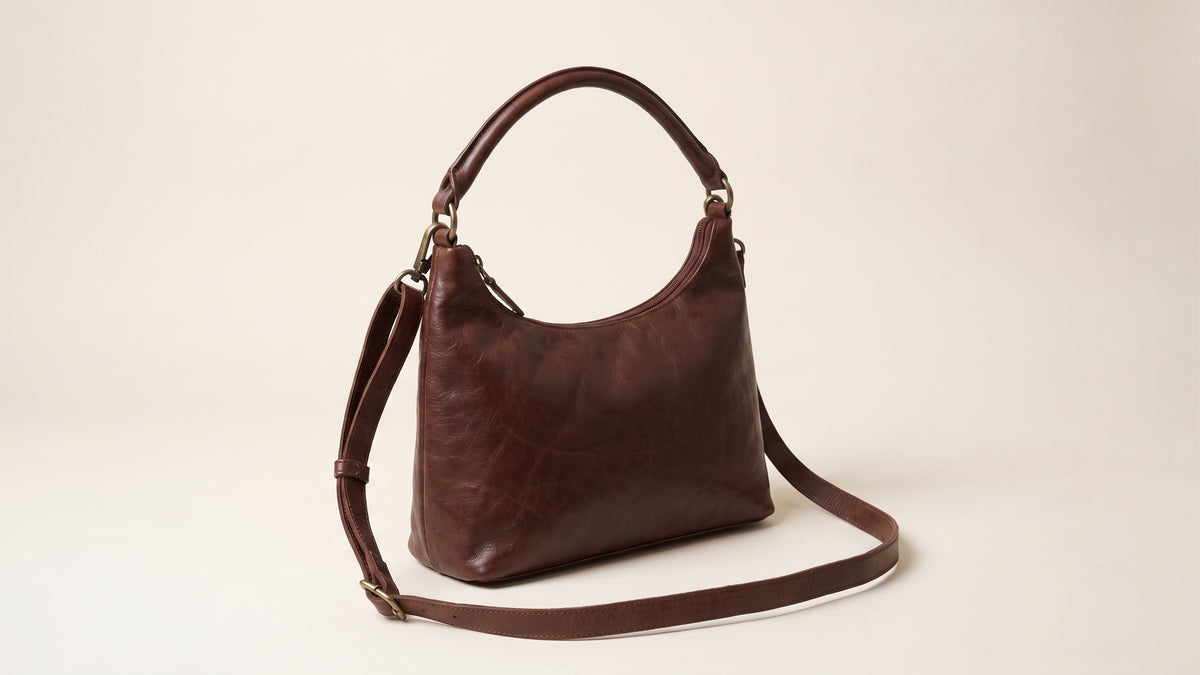 Brown leather handbag featuring an adjustable strap laid out on a marble surface