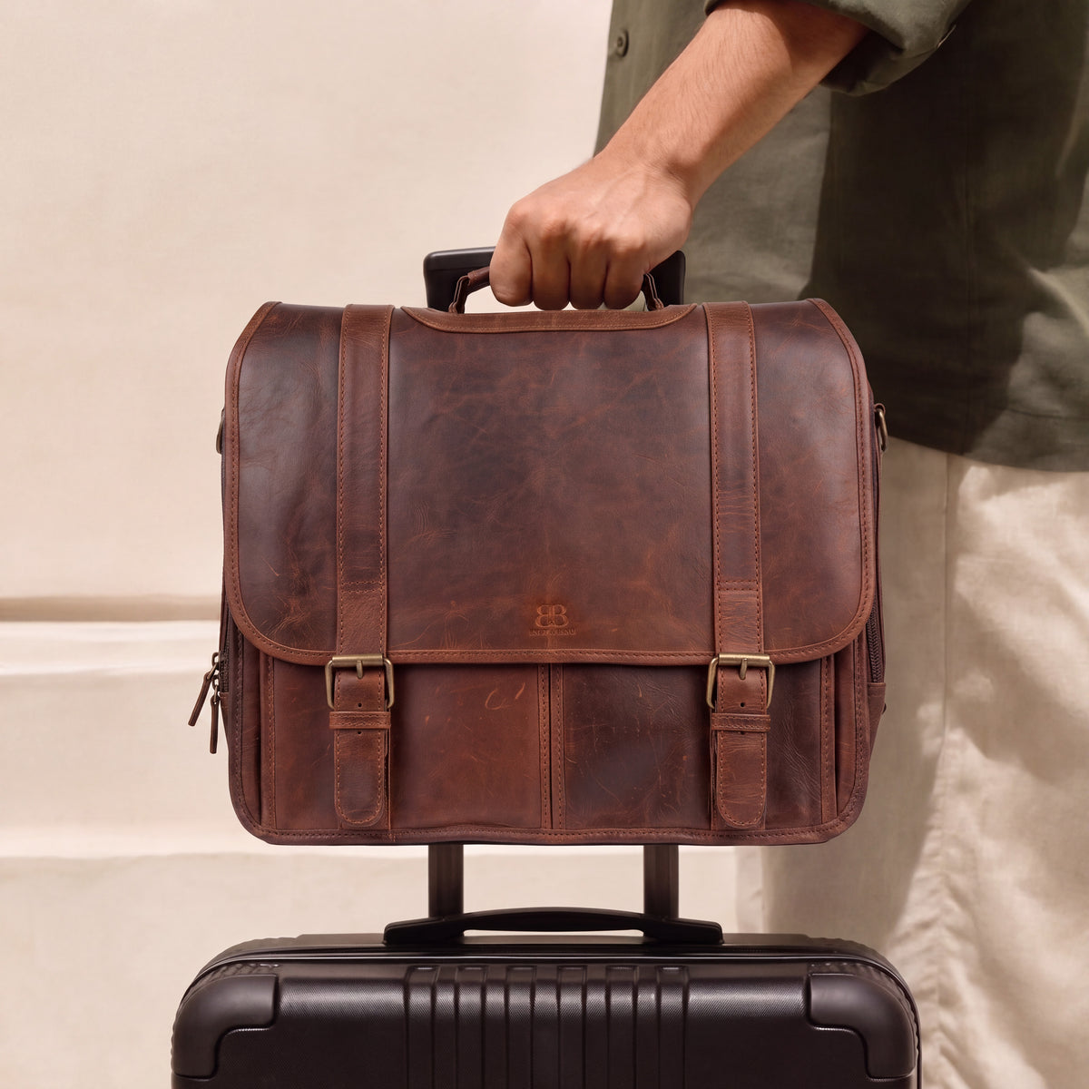 Man carrying brown leather briefcase attached to rolling luggage handle at airport