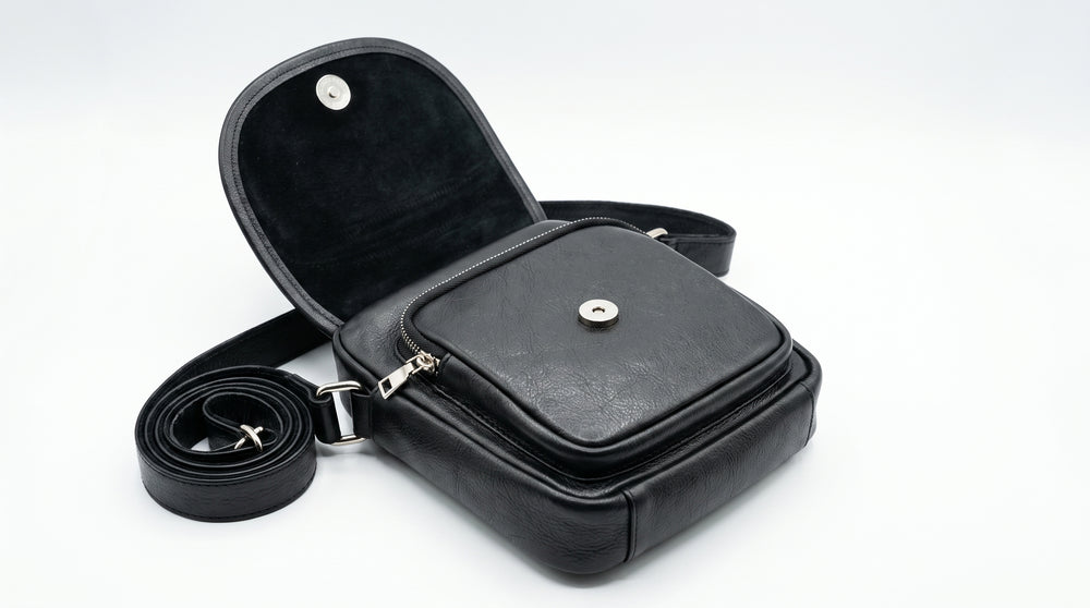 Open flap and magnetic button closure detail of black leather crossbody bag