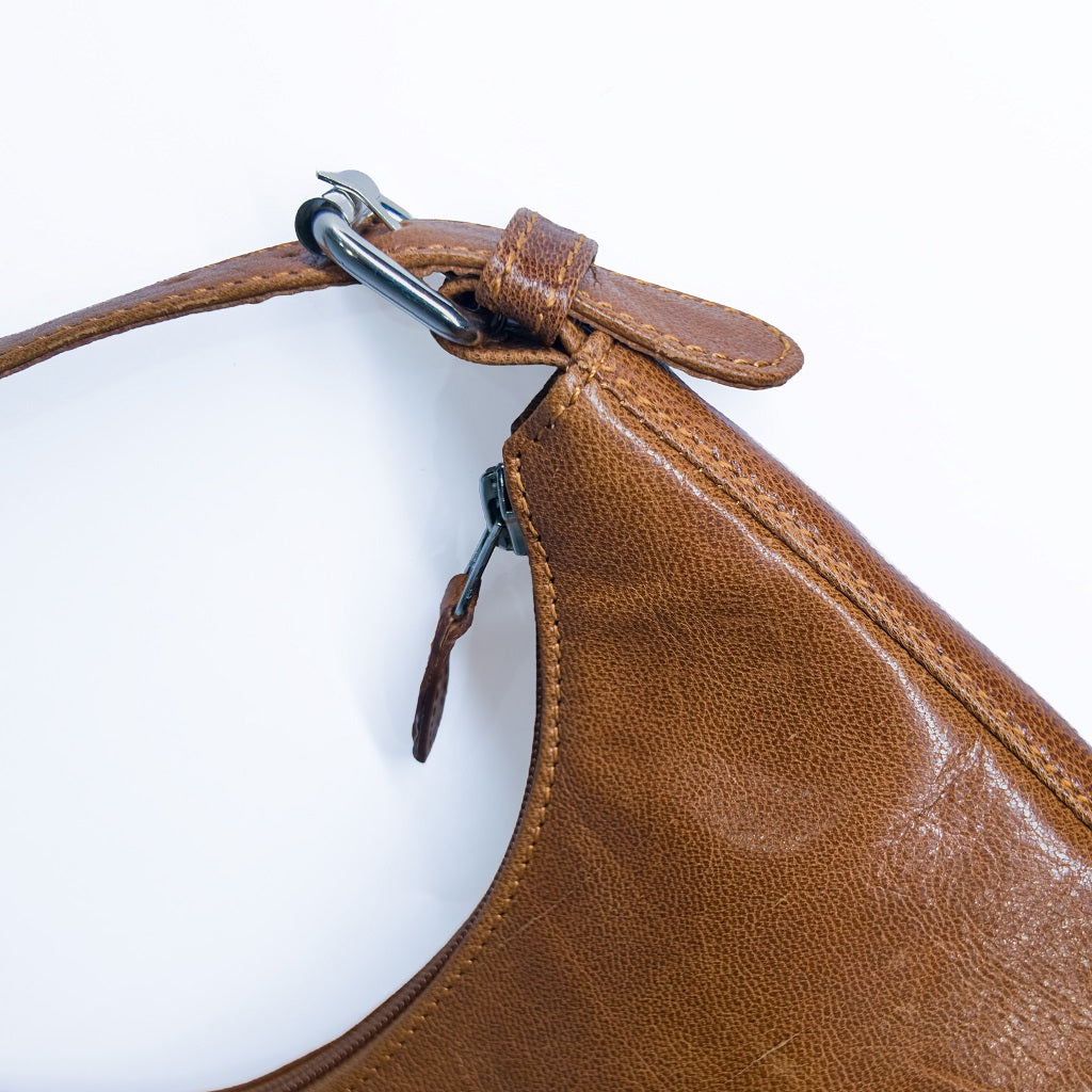 Close-up macro detail of the zipper and metal buckle on the tan leather handbag